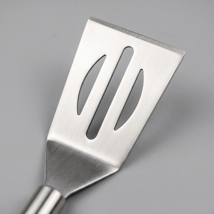 Close-up of a stainless steel grilling spatula, tongs, and fork from a 3-piece BBQ tool set with ergonomic long handles.