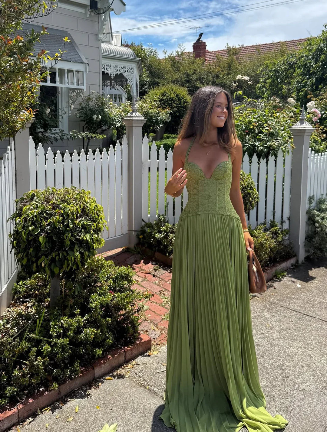 Formal women's pleated green maxi dress, featuring a halter neck & corset top, suited for wedding guests.
