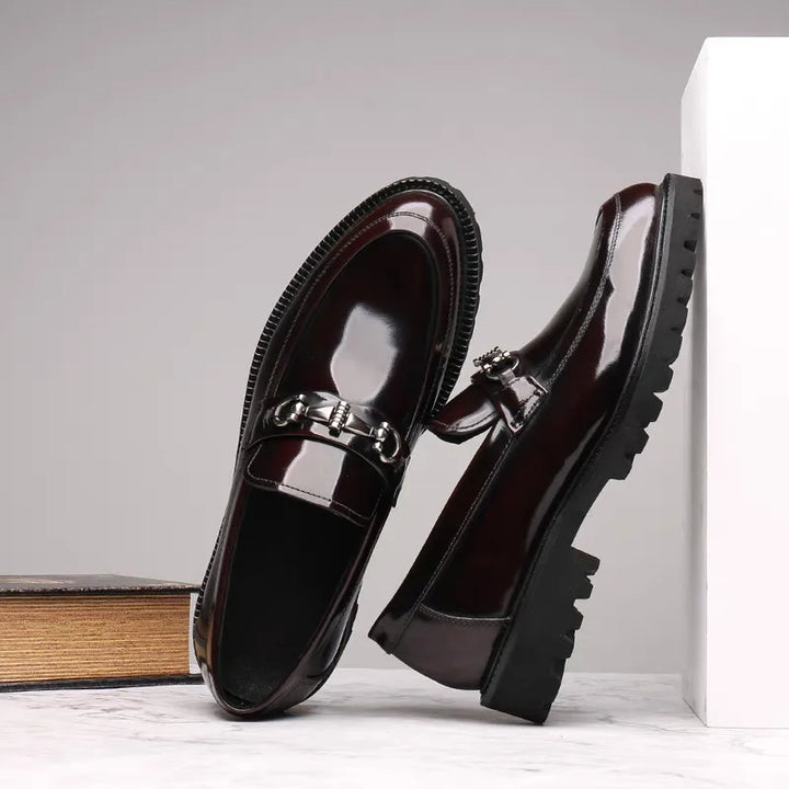 Men's burgundy polished loafers on feet, showcasing the elegant metal bit detail. Stylish formal footwear.