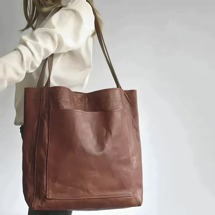 Women's oversized grained leather tote bag with large front pocket, perfect for work or travel.